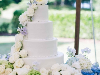 4 tier round pure white wedding cake with cascading roses 4 tier round pure white wedding cake decorated in white fondant with piped pearls edging where each tier meets the next. From the top to the bottom, the cake is decorated with cascading white roses with a grand display at the bottom.